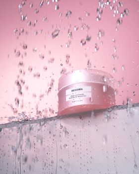 Pink cosmetic jar in shower with water droplets, vibrant lighting.