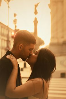 A romantic scene of a couple kissing on a city street with a sunset backdrop, casting a warm glow.