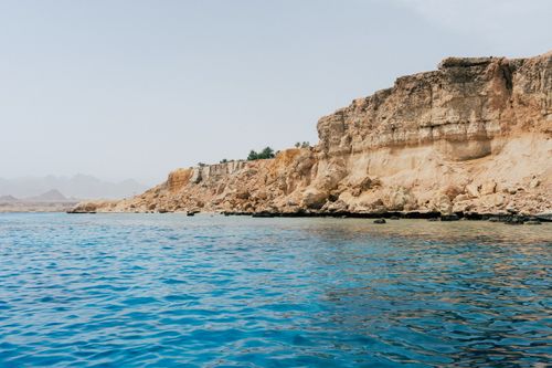 Free Breathtaking view of a towering cliff with clear blue ocean waters below, under a bright sky. Stock Photo