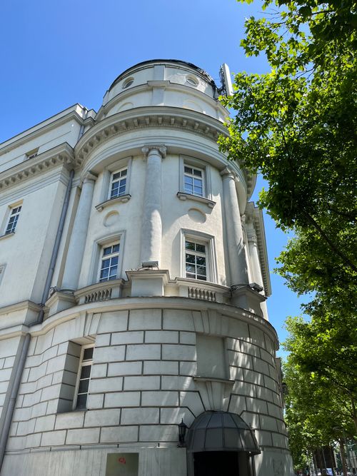 Free Low angle view of a classic exterior building against a clear blue sky, framed by green trees. Stock Photo