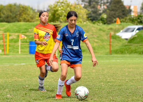 Two girls playing competitive soccer on a sunny day.