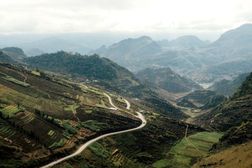 Free A beautiful mountain valley with winding road, lush greenery, and misty atmosphere. Stock Photo
