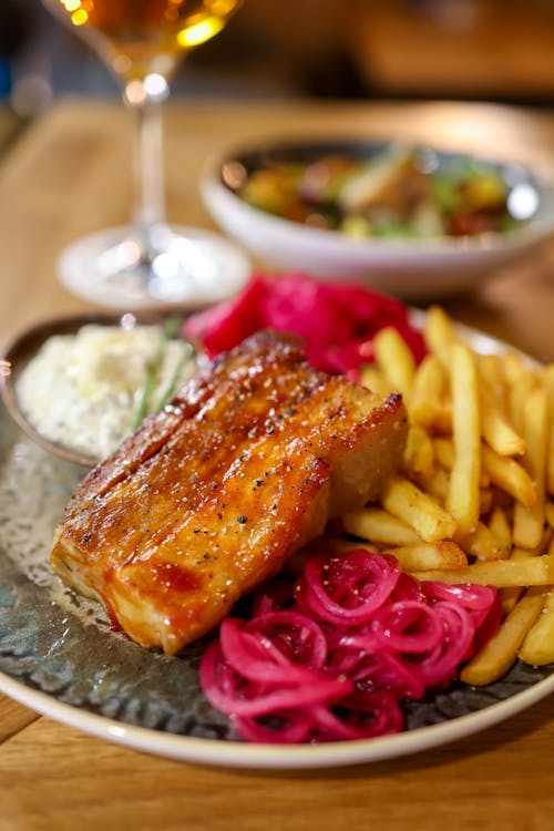 Free Mouthwatering pork belly with french fries and salad, served with wine. Stock Photo