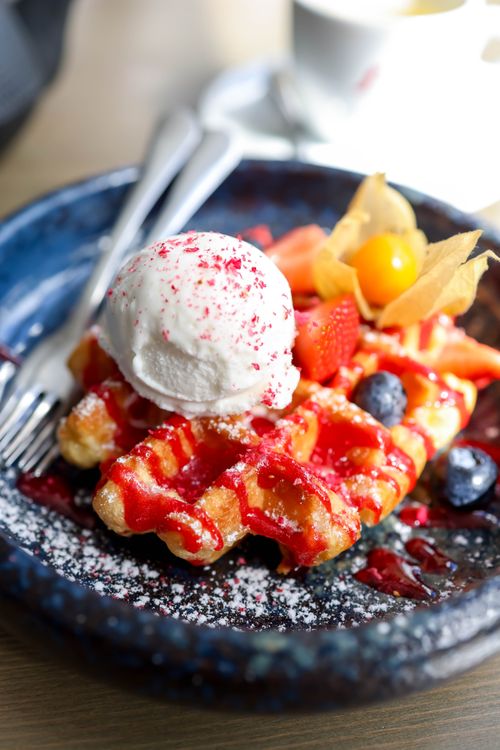 Free Appetizing waffle dessert topped with ice cream, strawberries, blueberries, and syrup on a plate. Stock Photo