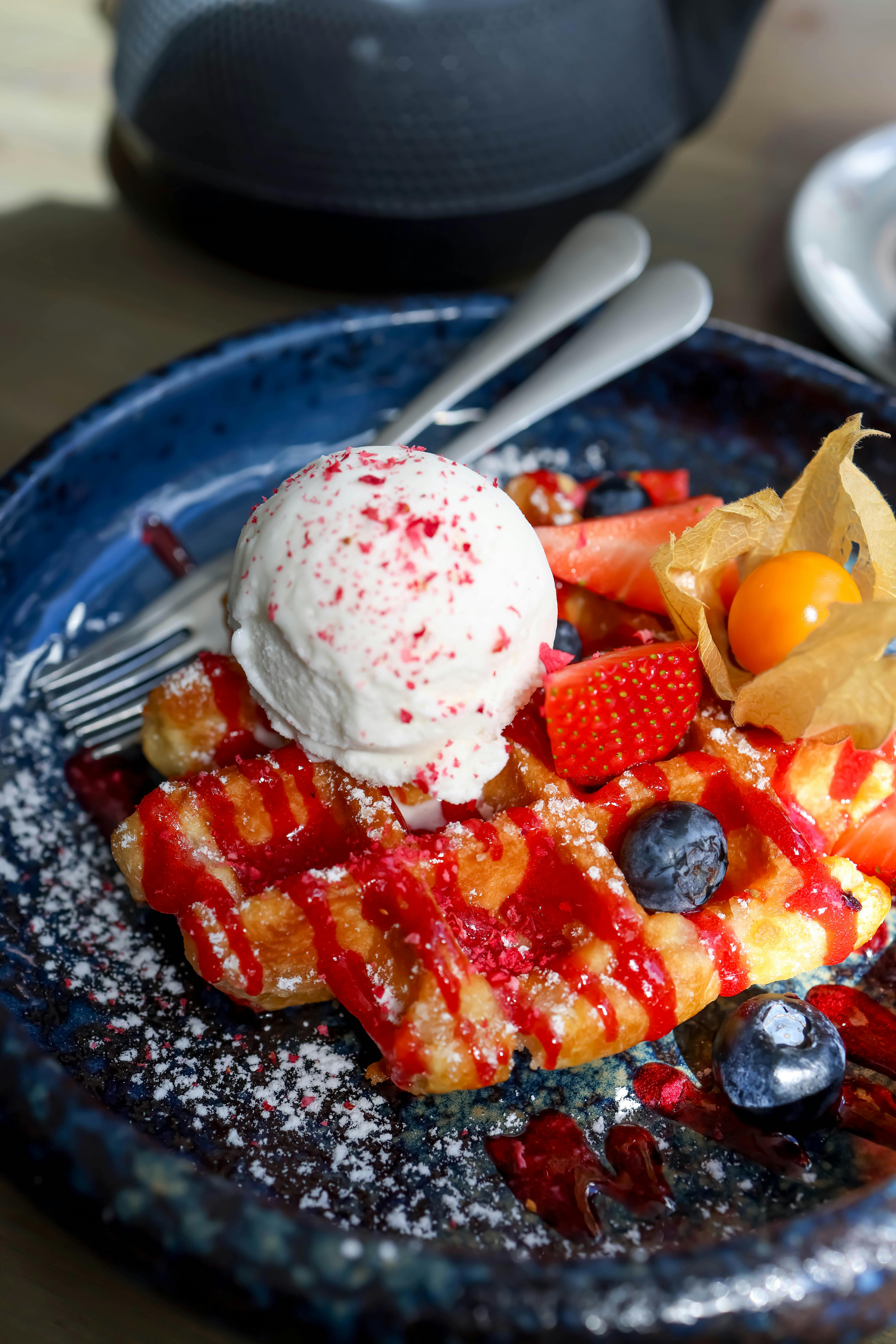 Mouth-watering waffle dessert topped with ice cream, strawberries, blueberries, and a ground cherry.
