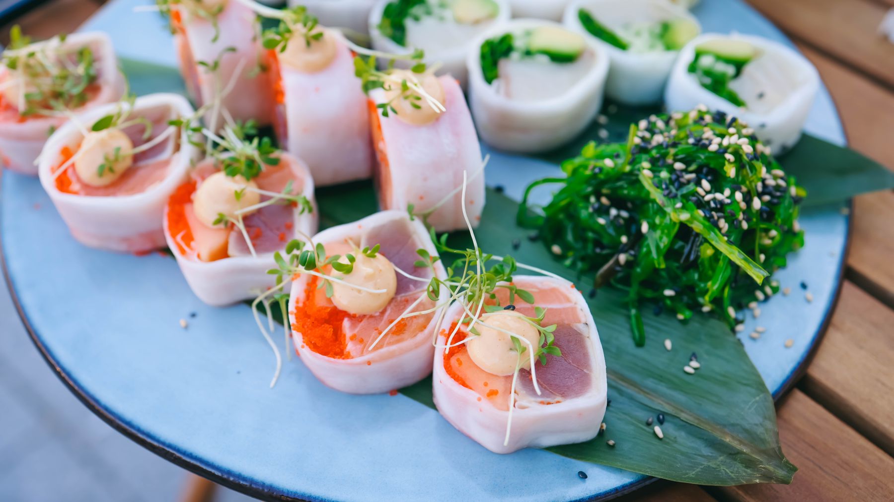 Close-up of vibrant sashimi rolls with seaweed salad on a blue plate, showcasing Japanese cuisine.