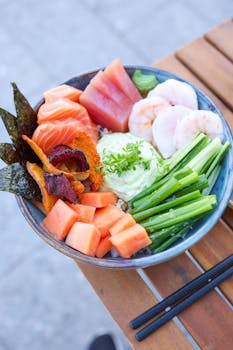 A colorful poke bowl featuring salmon, tuna, shrimp, papaya, and greens artistically arranged.
