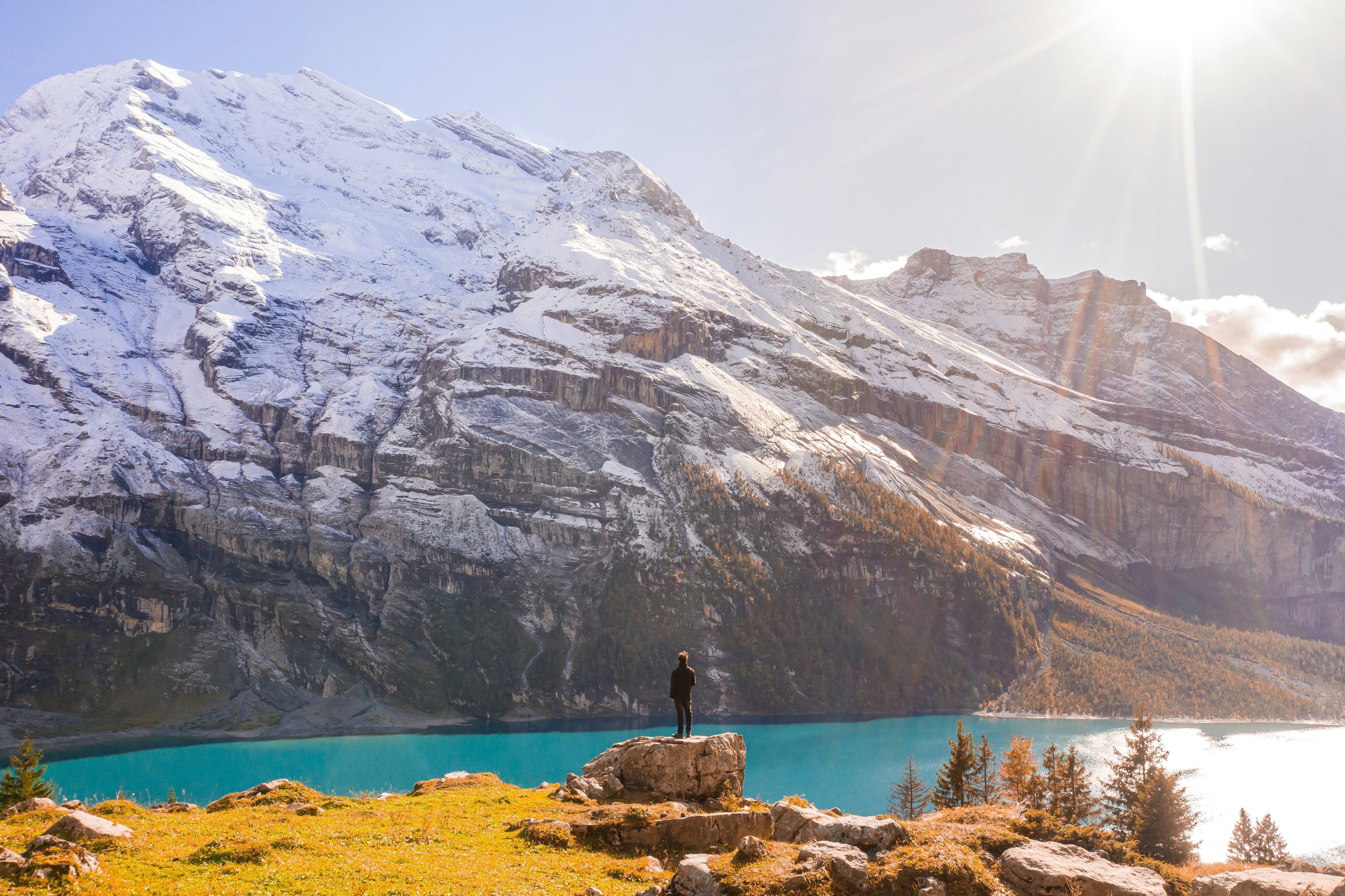 A person stands on a rock with a stunning view of the snowcapped Swiss Alps and Oeschinen Lake.