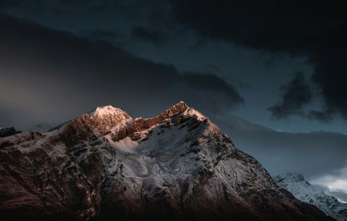 Free Breathtaking view of a snowcapped mountain peak illuminated by dawn light under dramatic skies. Stock Photo