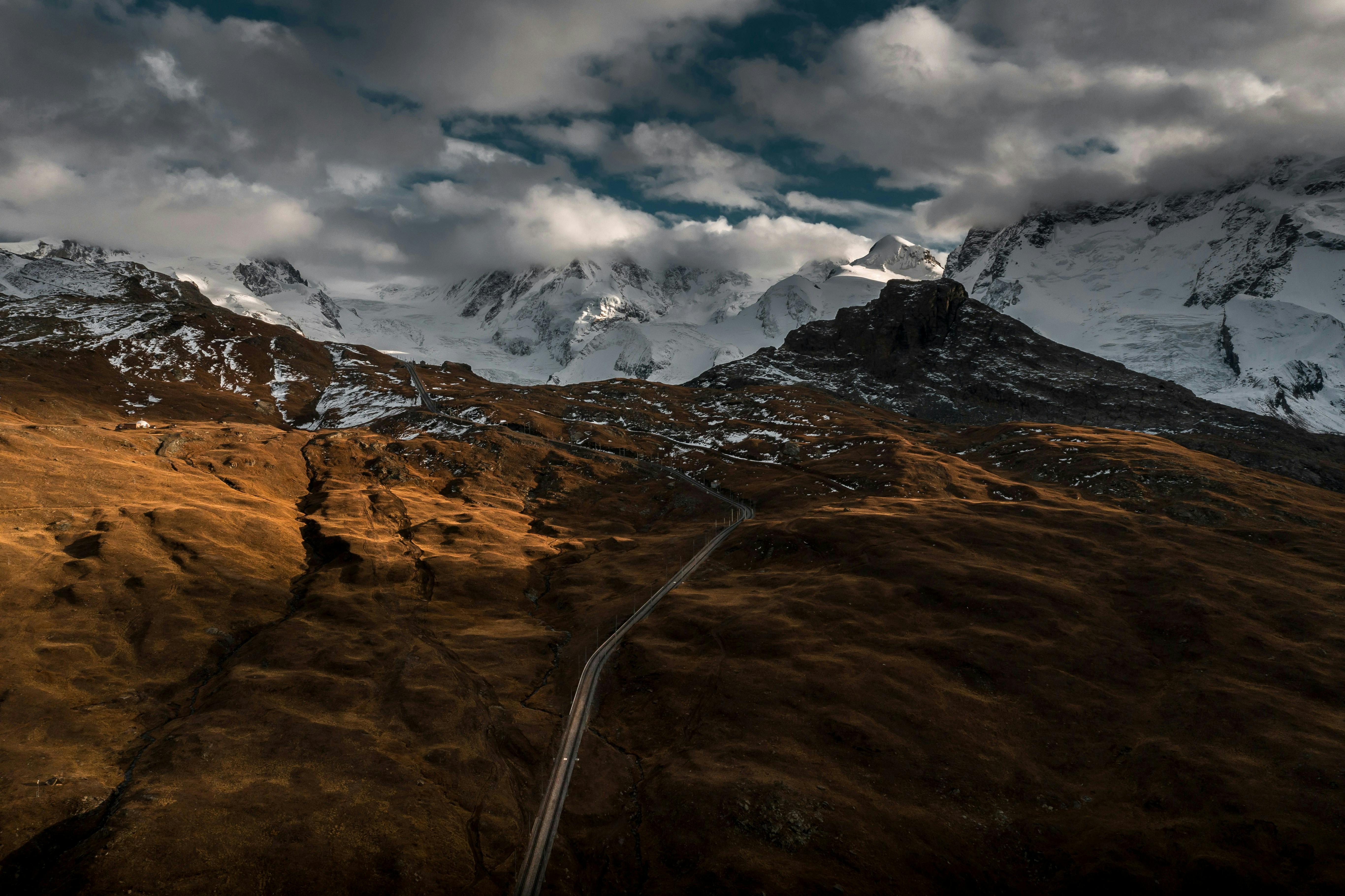 Breathtaking view of snowcapped mountains and winding road under dramatic skies.