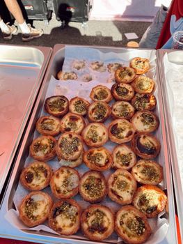 Tray of freshly baked mini pastries with herbs displayed outdoors, perfect for food events.