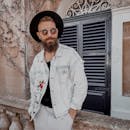 一位留着胡须、穿着牛仔夹克、戴着太阳镜的时尚男子在户外