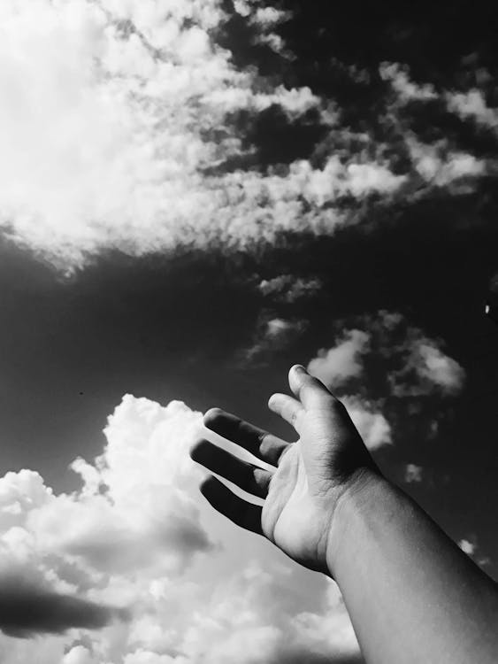 Grayscale Photo Of Person Raising Hands Towards the Sky