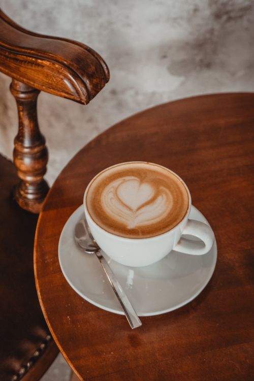 Free A cappuccino cup with heart latte art on a rustic wooden table and chair. Stock Photo