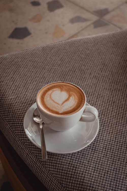 Free A cup of cappuccino with heart-shaped froth art on a saucer with a spoon. Stock Photo