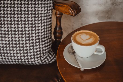A cup of captivating latte art sitting by a wooden armchair, offering a warm and inviting mood.