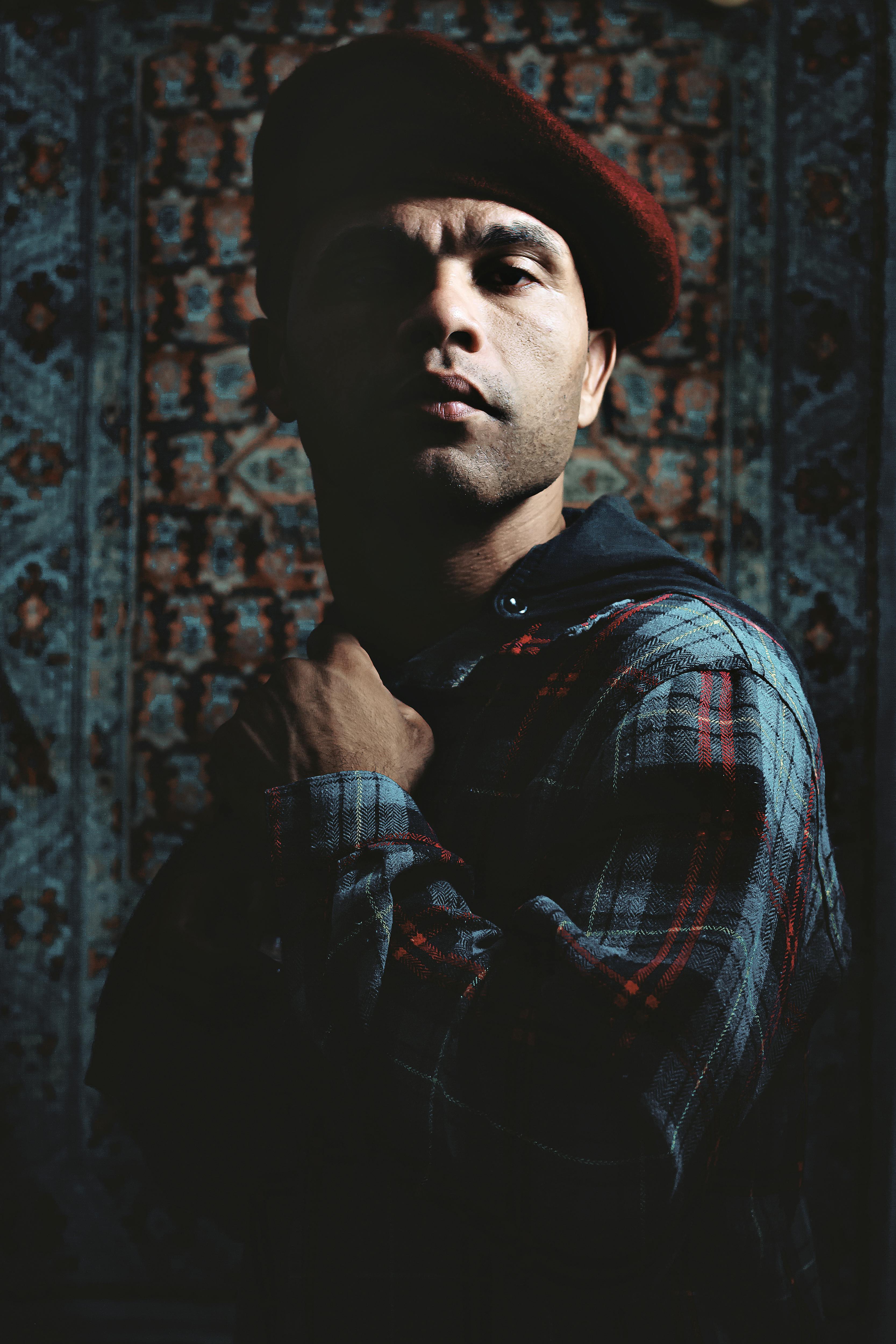 Serious bearded ethnic male in checkered shirt and red beret standing in dark place and looking at camera confidently