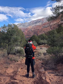 一名徒步旅行者背着背包，在一条红色岩石遍布、天空晴朗的沙漠小道上，享受着风景优美的徒步之旅