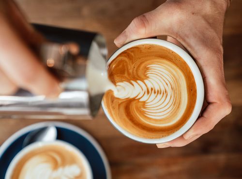 Free Close-up of barista pouring milk creating intricate latte art in coffee cup. Stock Photo