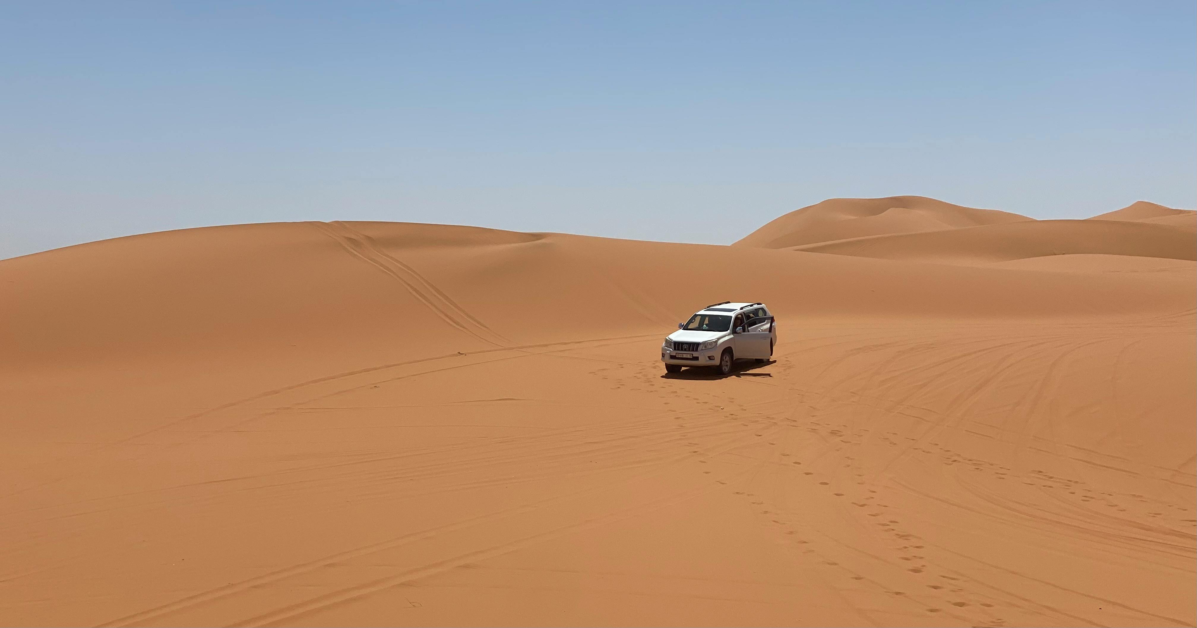 A 4x4 SUV driving through sandy desert dunes under a clear sky.