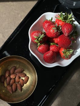 Bowl of fresh strawberries and almonds on a tray, captured in natural sunlight.