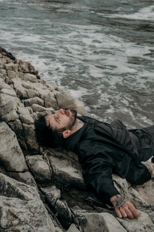 A man laying on the rocks by the ocean