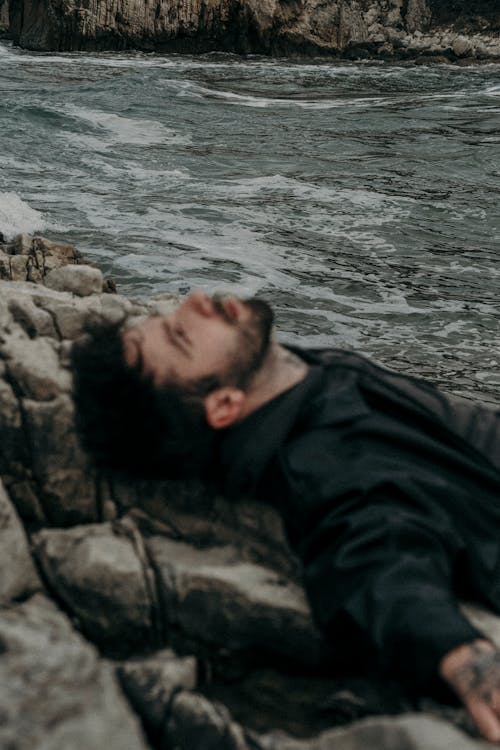 A man laying on the rocks by the ocean