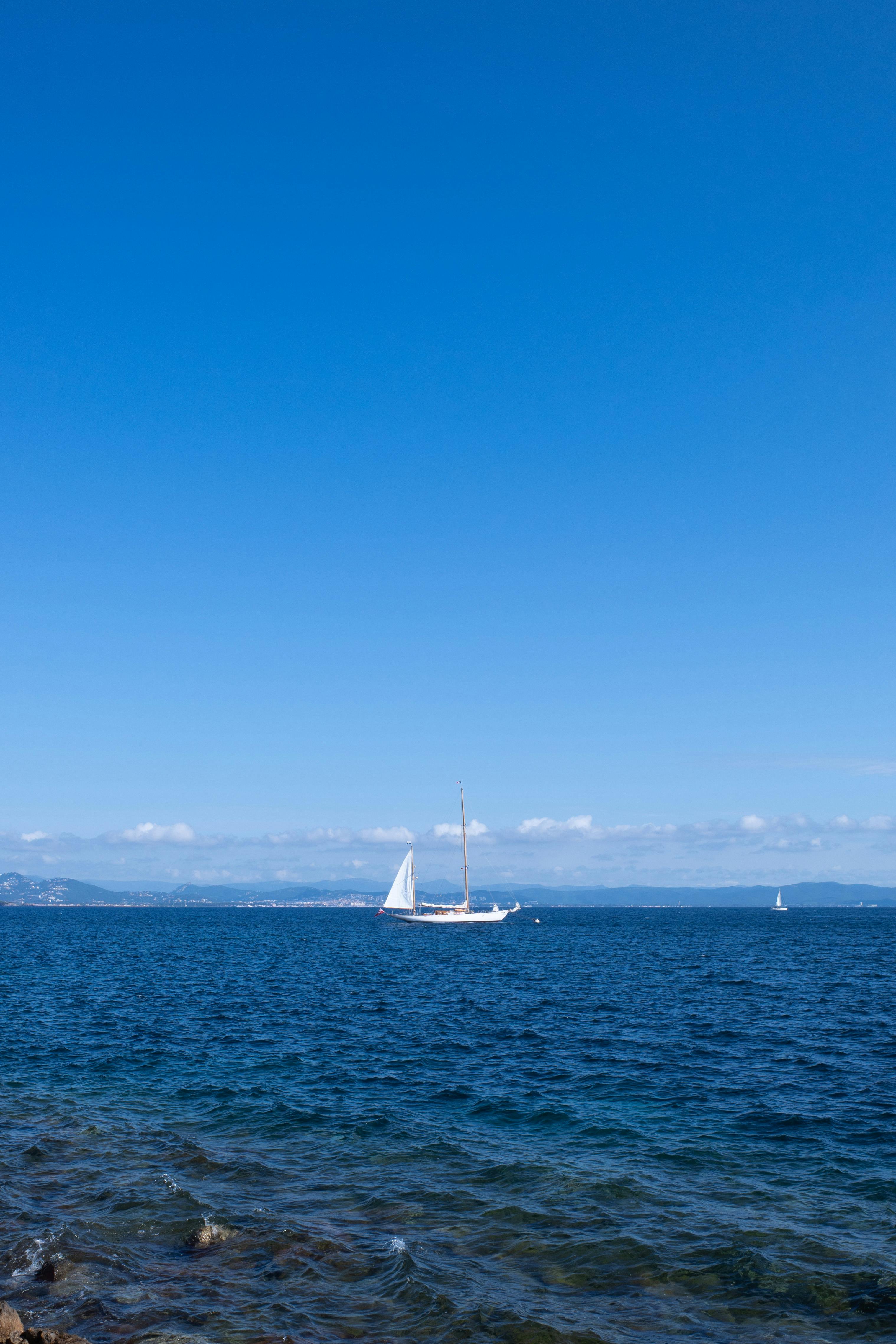 A sailboat drifts peacefully on a calm ocean under a clear summer sky, evoking tranquility.