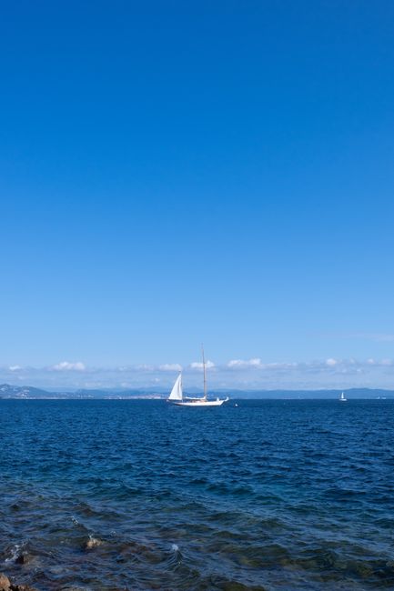 A sailboat drifts peacefully on a calm ocean under a clear summer sky, evoking tranquility.