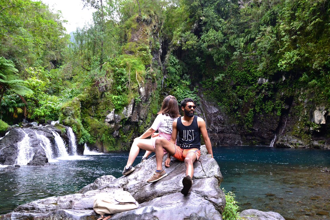 Couple Sitting On Rock Near Body Of Water