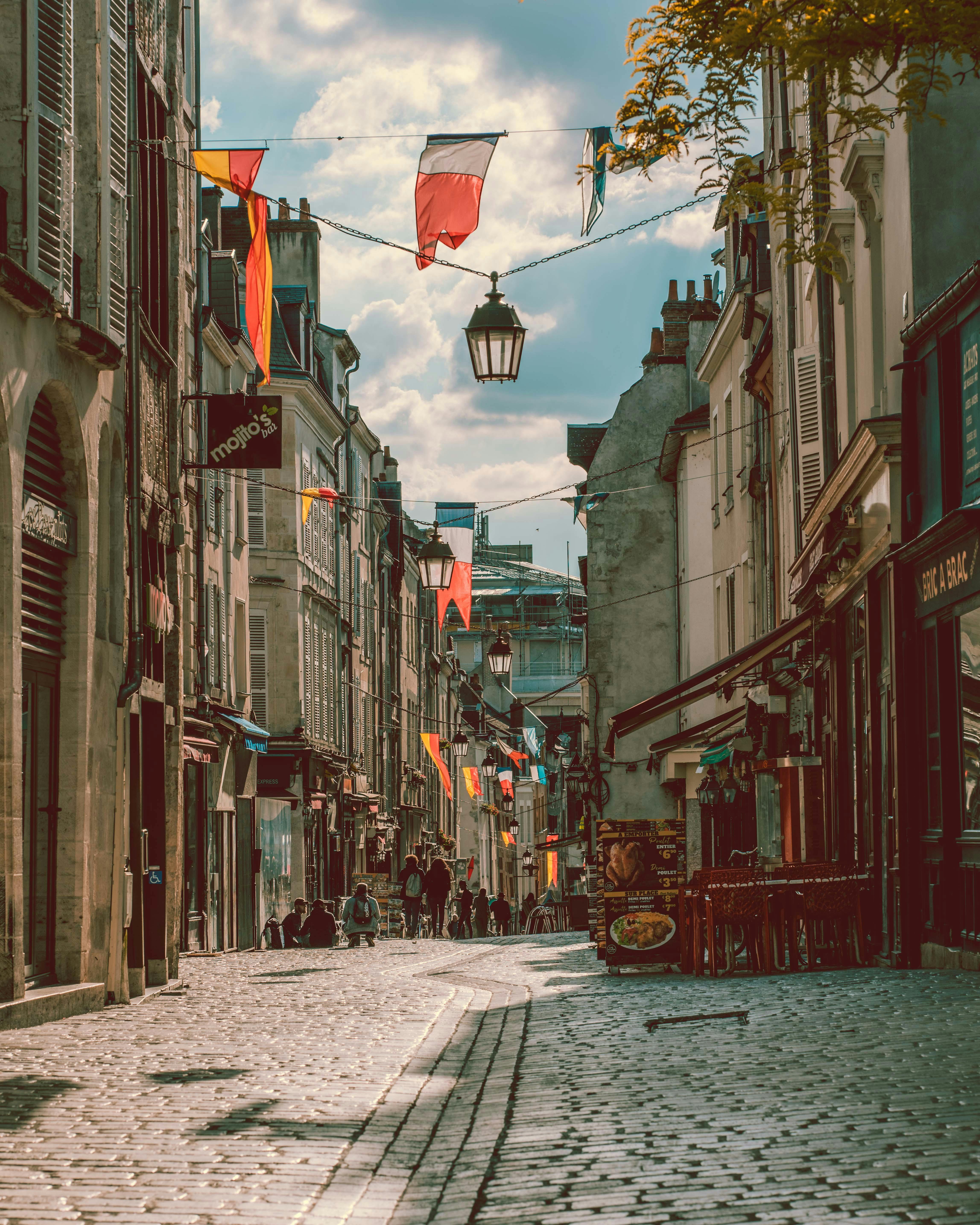 法国奥兰的鹅卵石街道两旁排列着古老的建筑和彩色的旗帜，风景如画