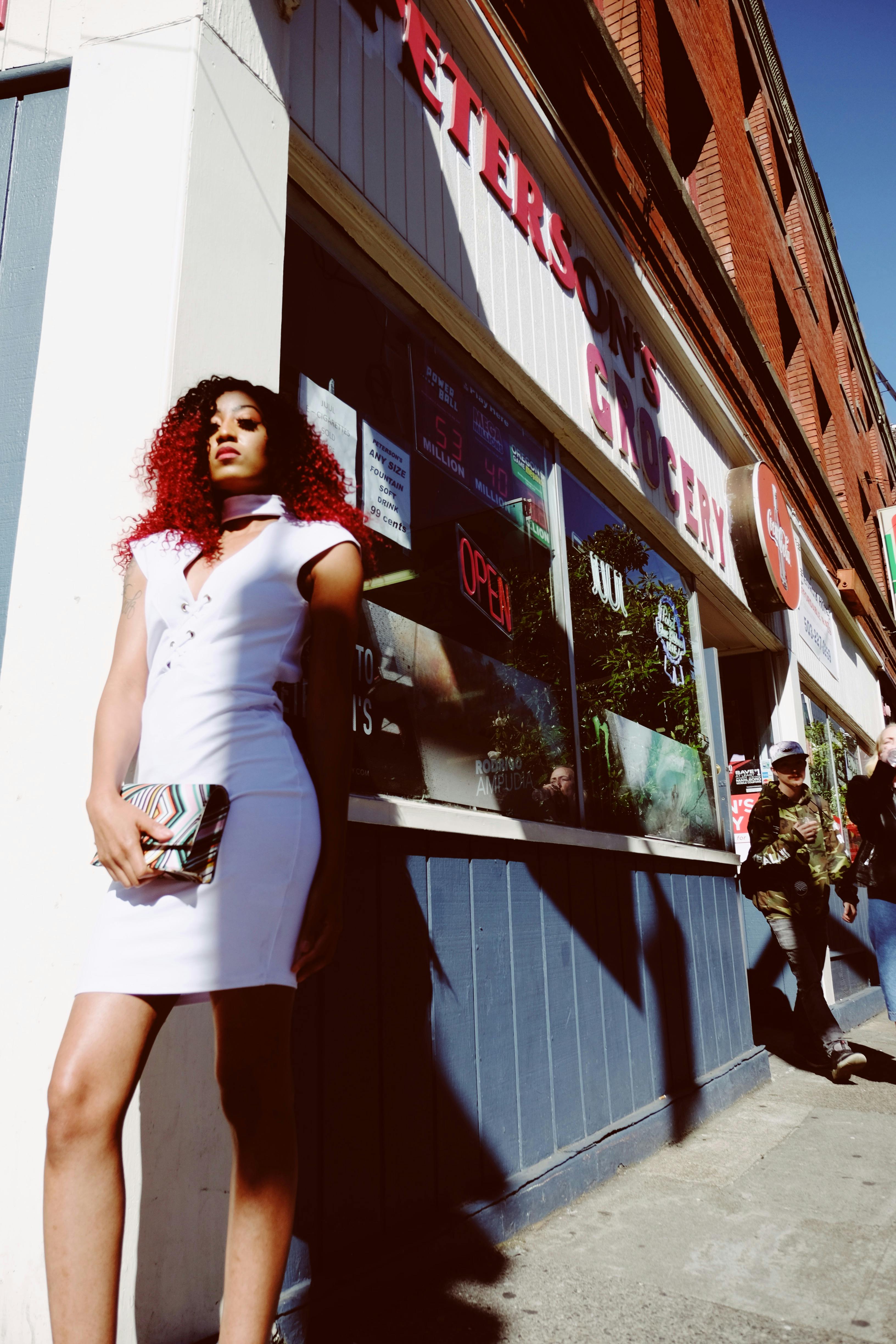 A stylish woman in a white dress poses confidently outside an urban grocery store, capturing the essence of street fashion.