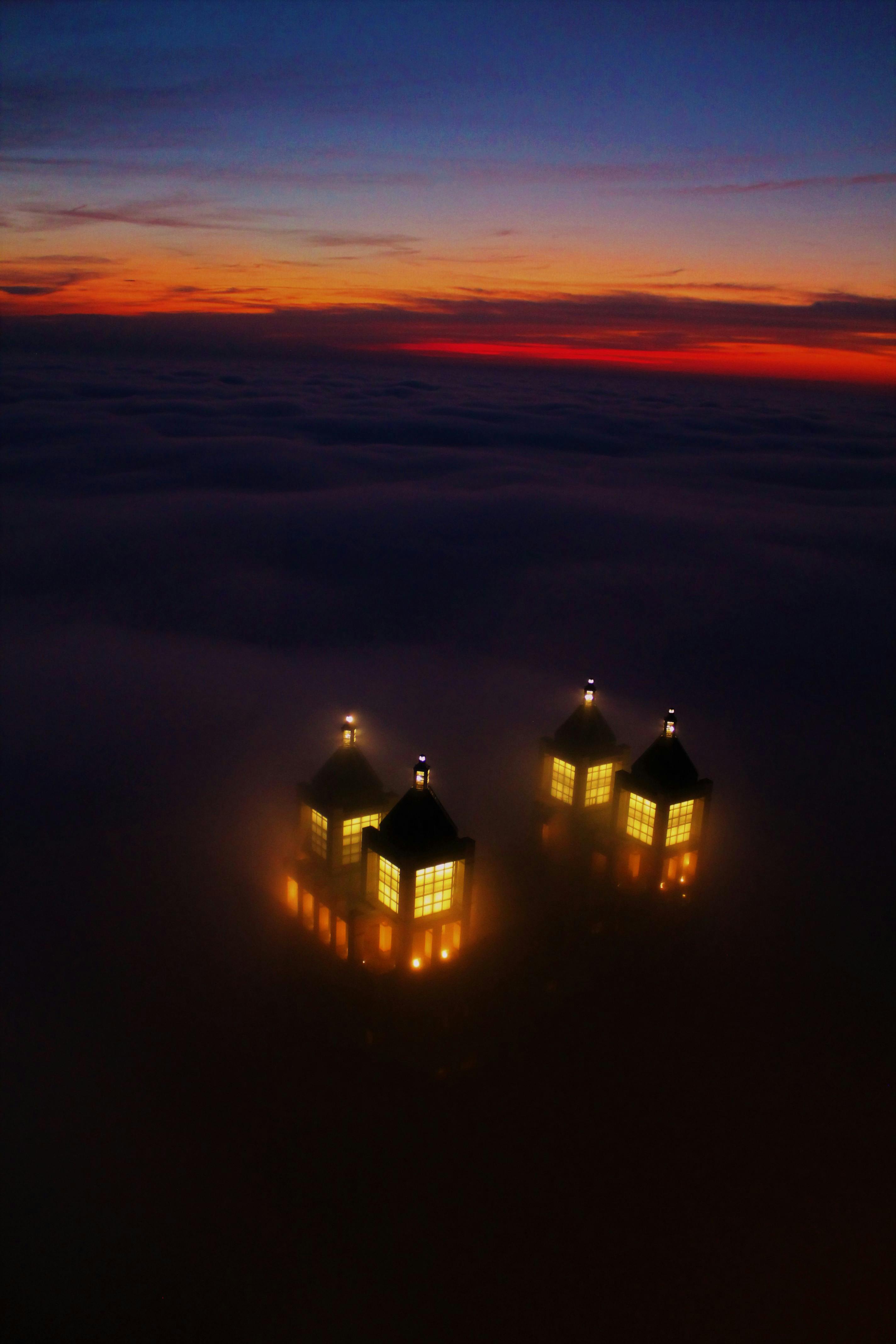 日落时分，从雾中浮现出发光塔楼的超现实鸟瞰图，营造出一片神秘的风景