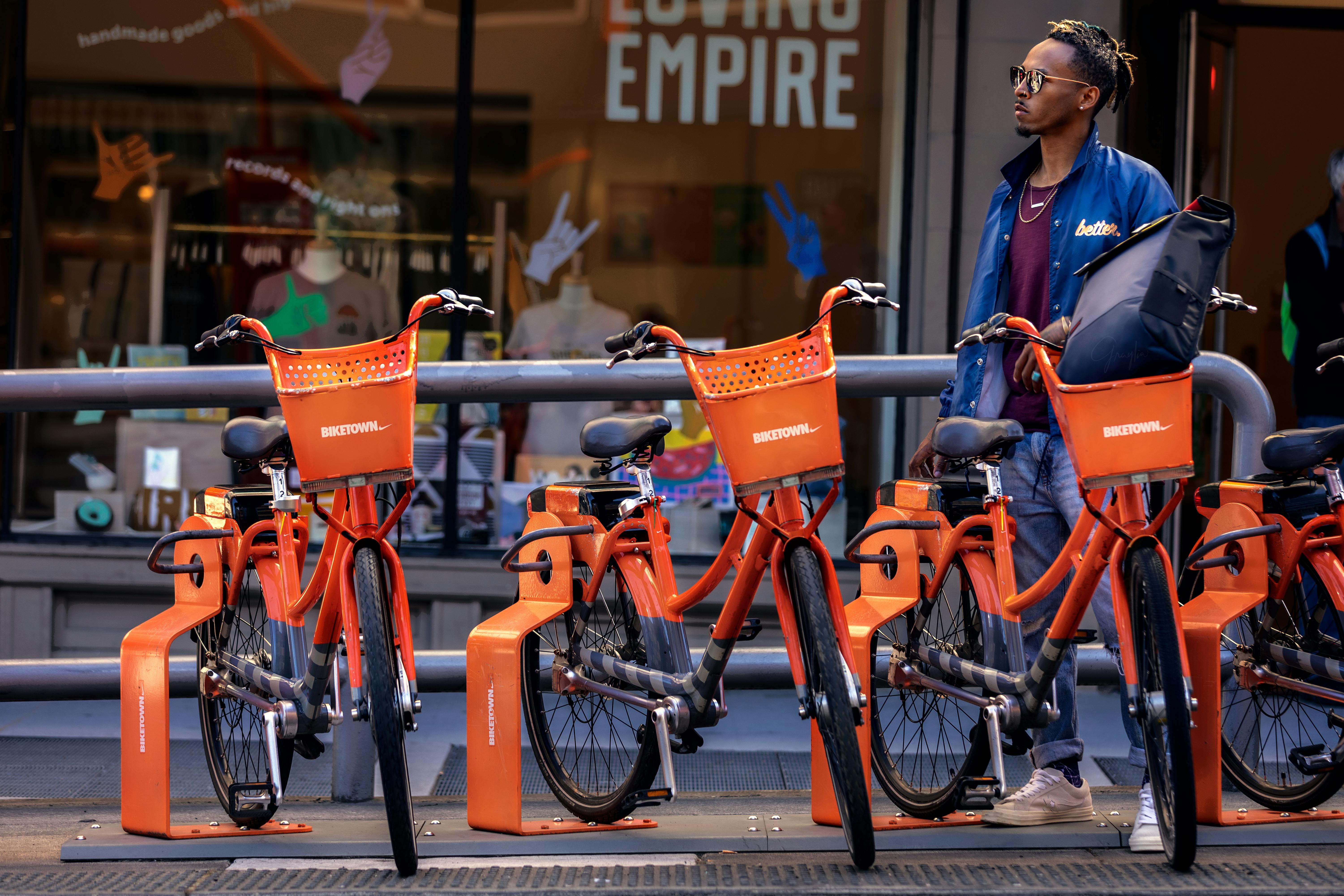 Man standing by orange Biketown rental bikes in Portland, Oregon.