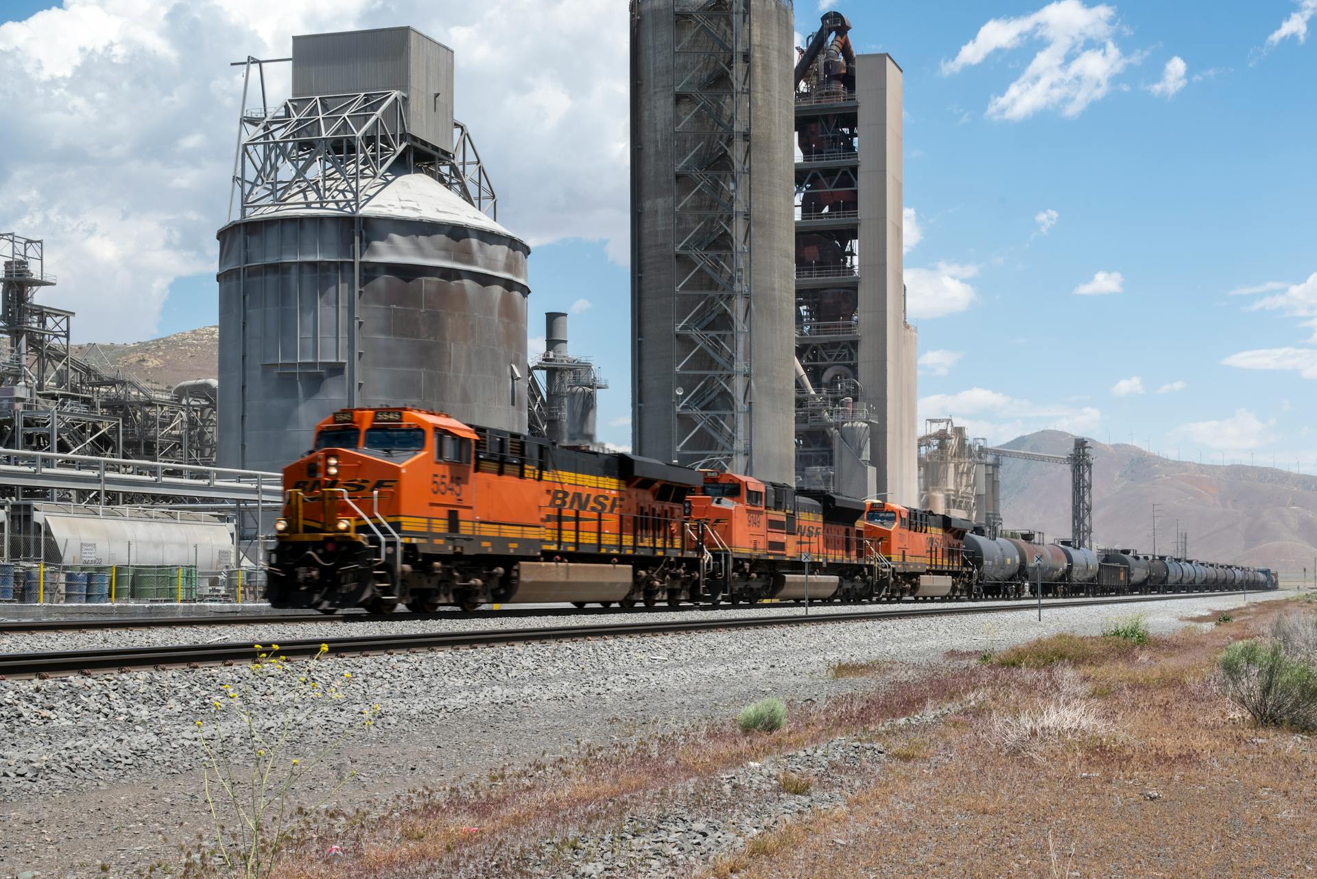 BNSF freight train passing a cement factory in Monolith, California with blue skies overhead.