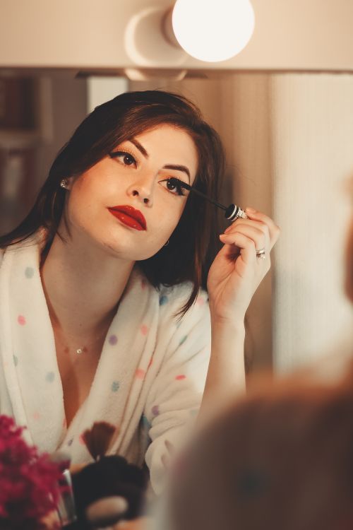 Free Glamorous woman applying mascara in front of a vanity mirror, enhancing her beauty. Stock Photo