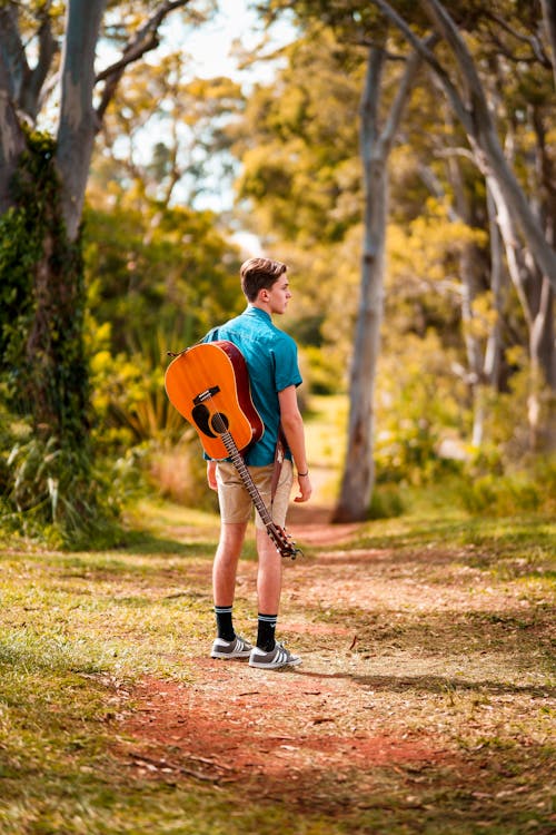 Back View Photo of Man Acoustic Carrying Guitar Standing Alone on Trail Looking to His Right