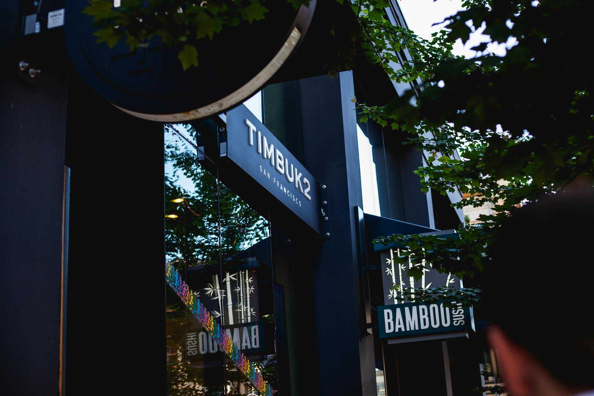 View of modern storefronts in a vibrant urban area featuring Timbuk2 and Bambou signage.