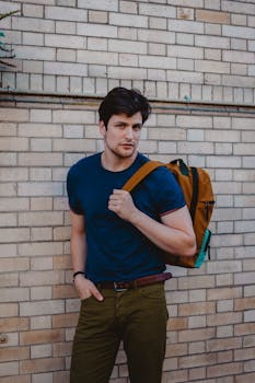 一名穿着蓝色衬衫、背着背包的男子随意地靠在砖墙上