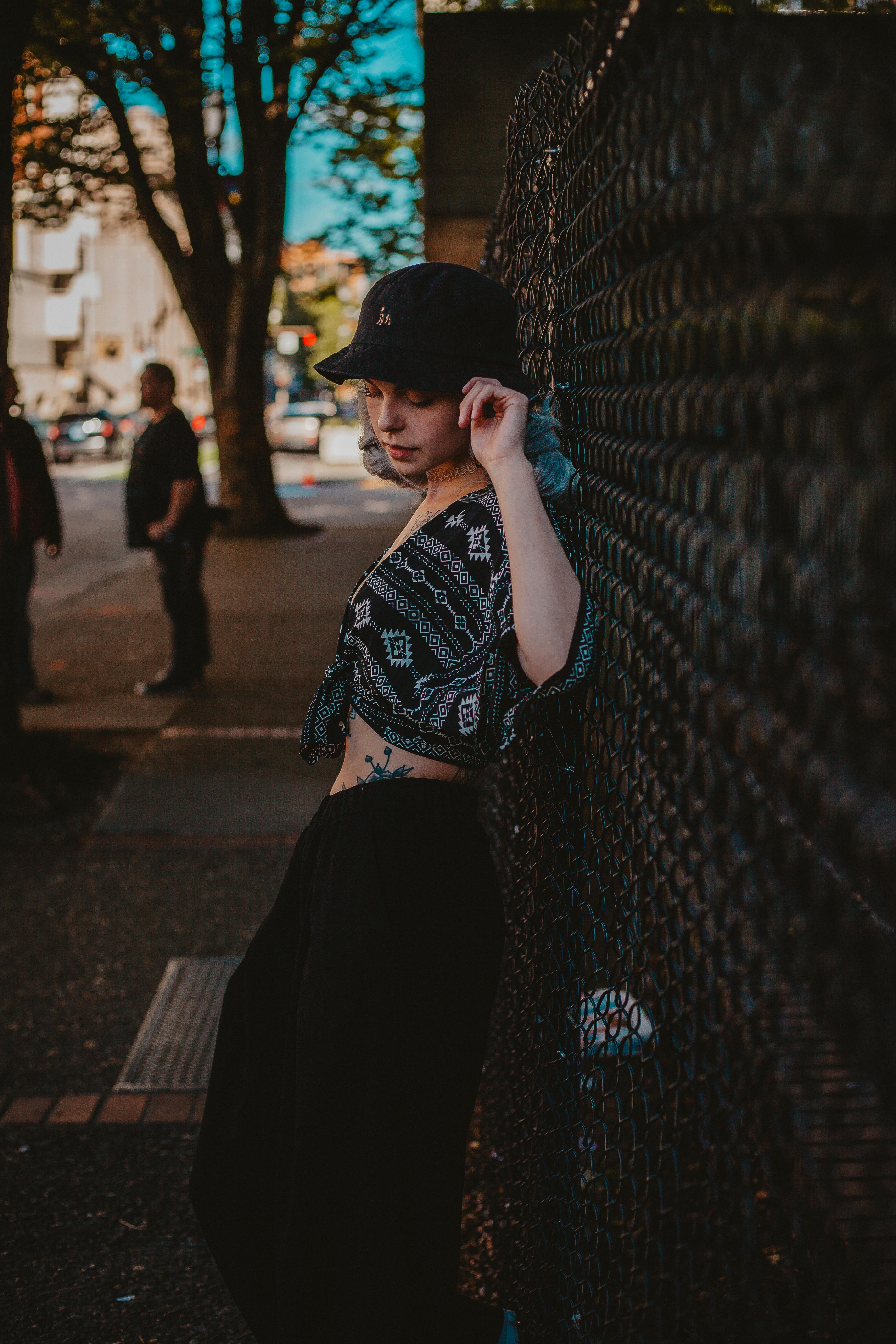 Portrait of a woman in casual wear leaning on a chain link fence in an urban setting.