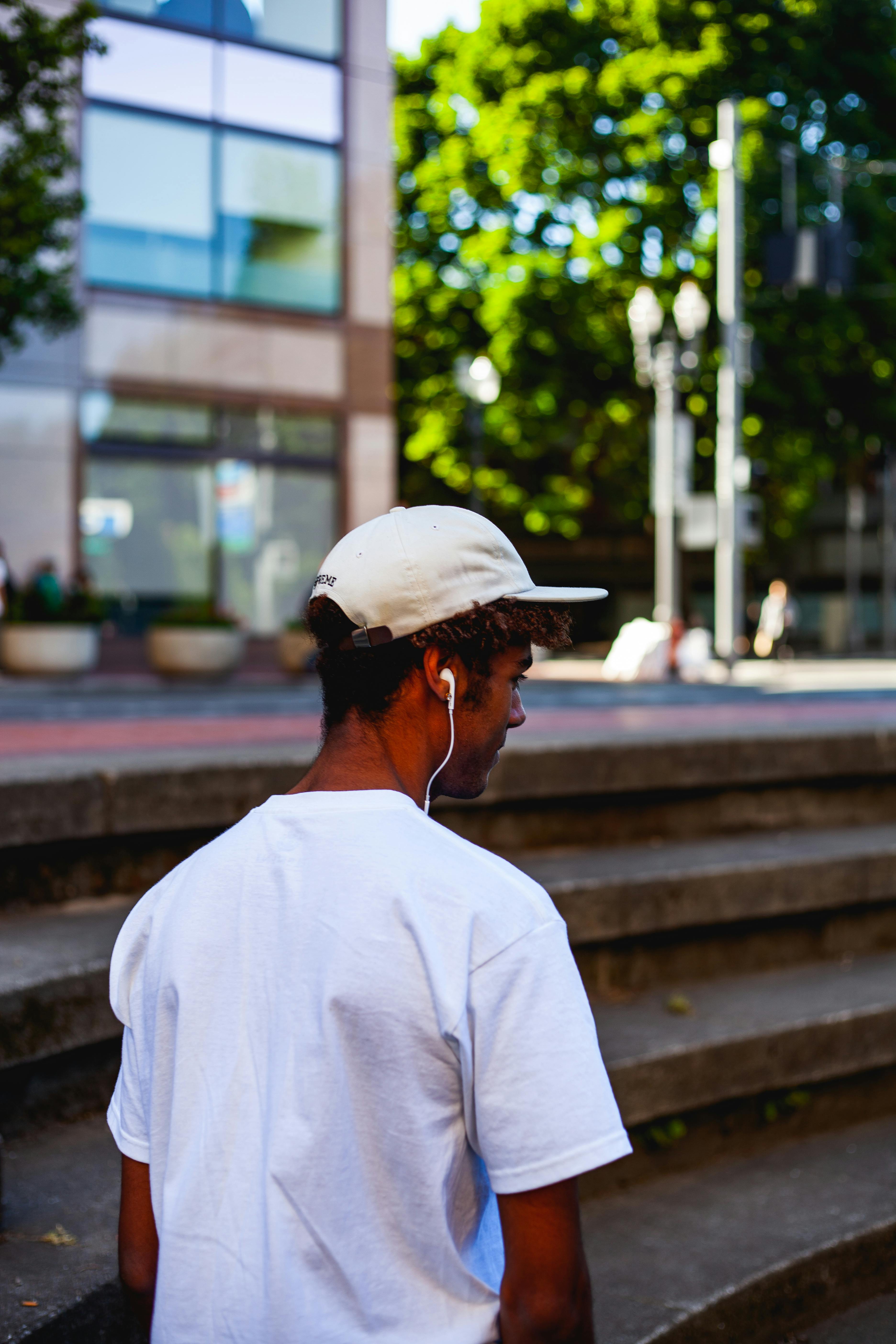 Young man in urban setting wearing a cap and headphones, enjoying sunny day outdoors.