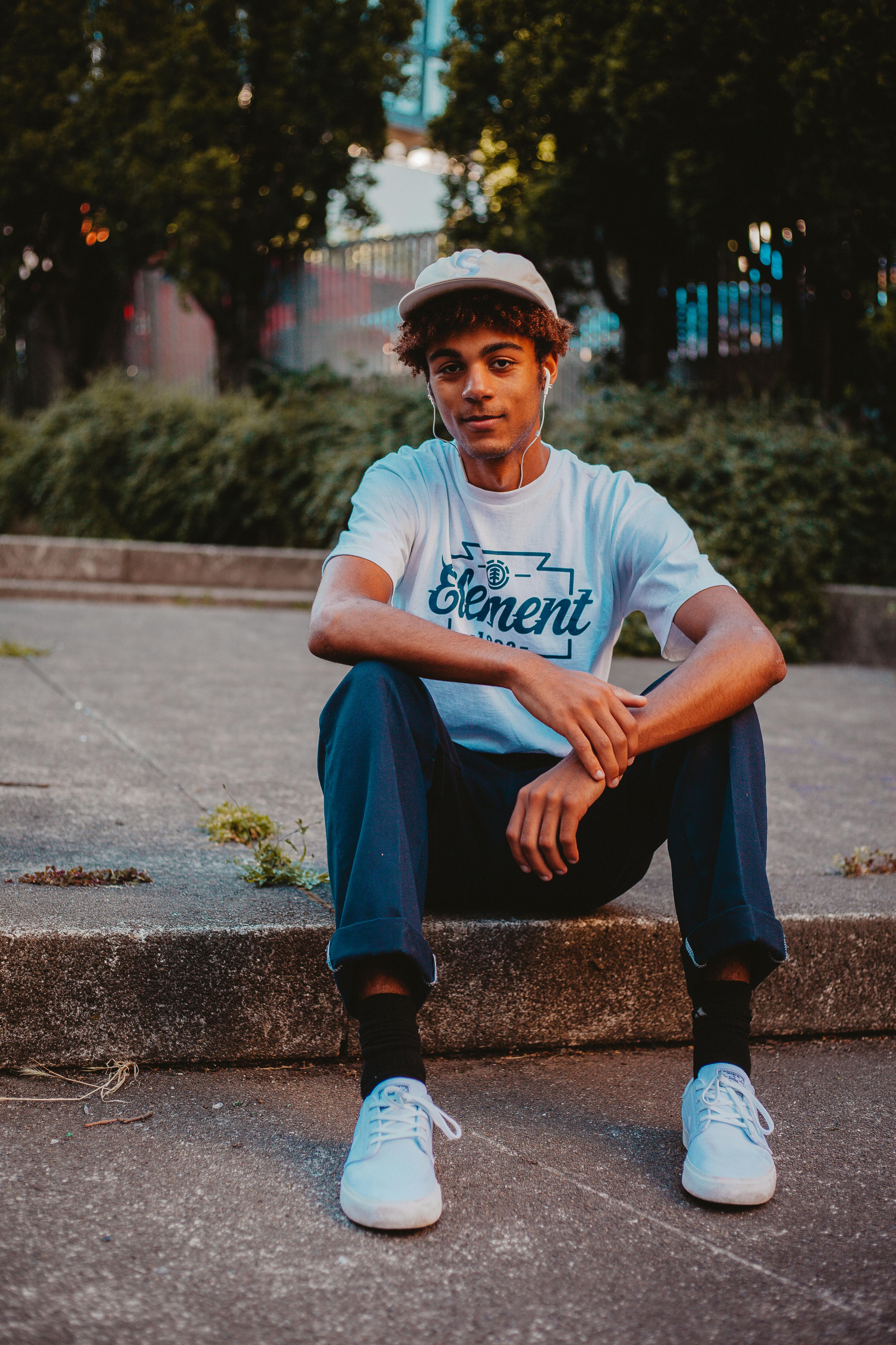 Casual young man sitting on a curb enjoying a relaxed moment outdoors.