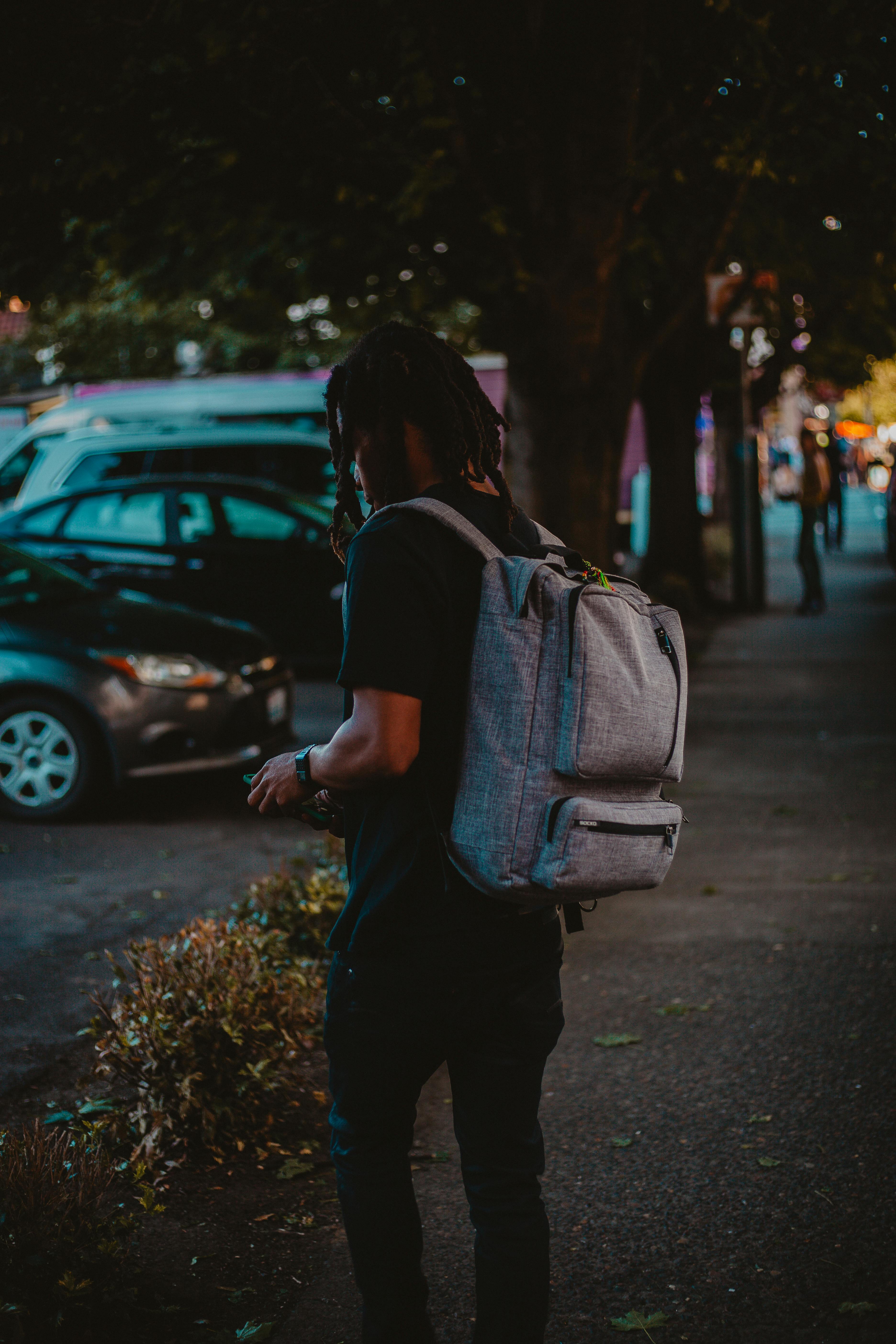 A person carrying a backpack strolling down a dimly lit city street.