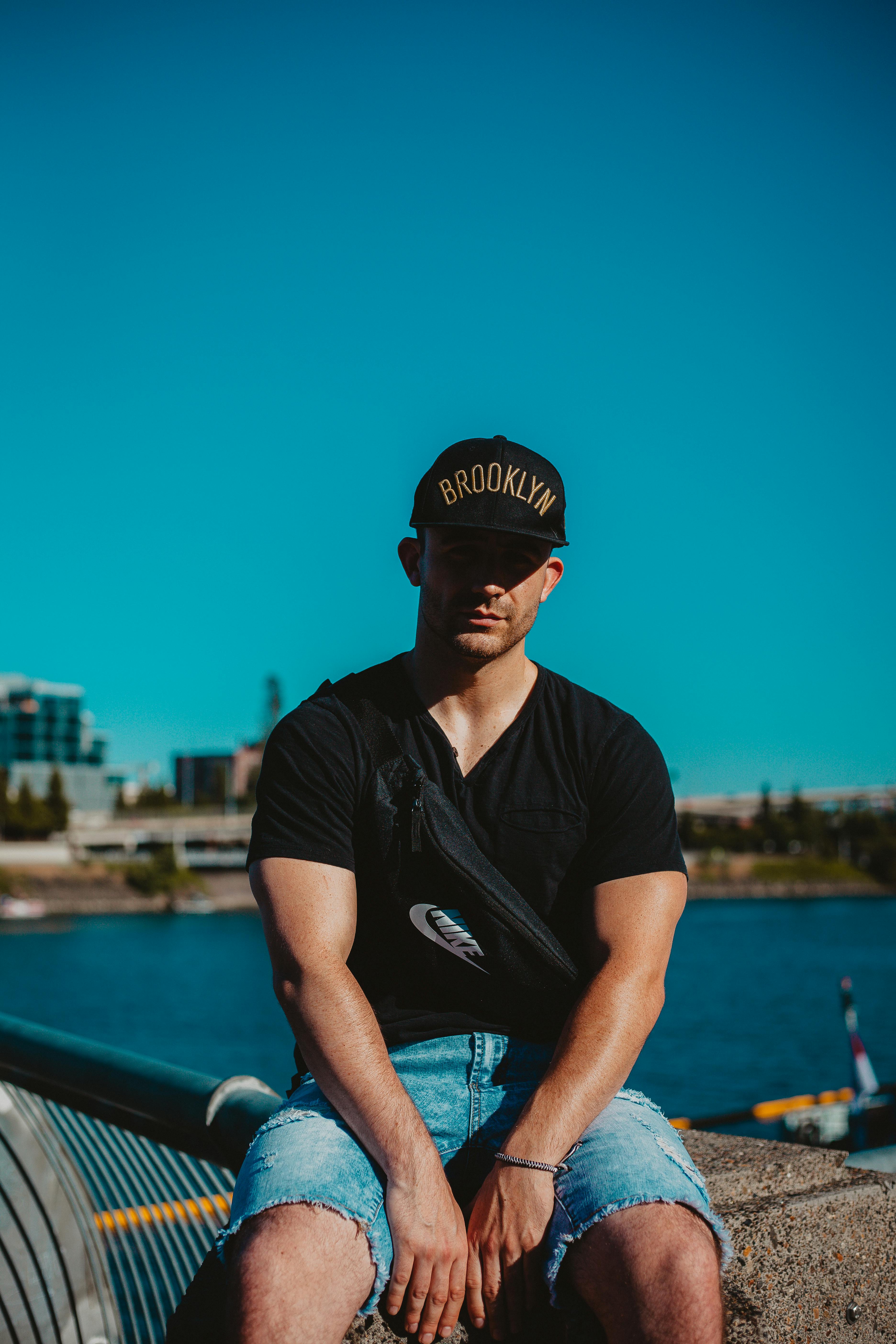 阳光明媚，一名穿着休闲装、戴着布鲁克林帽子的男子在河边摆姿势