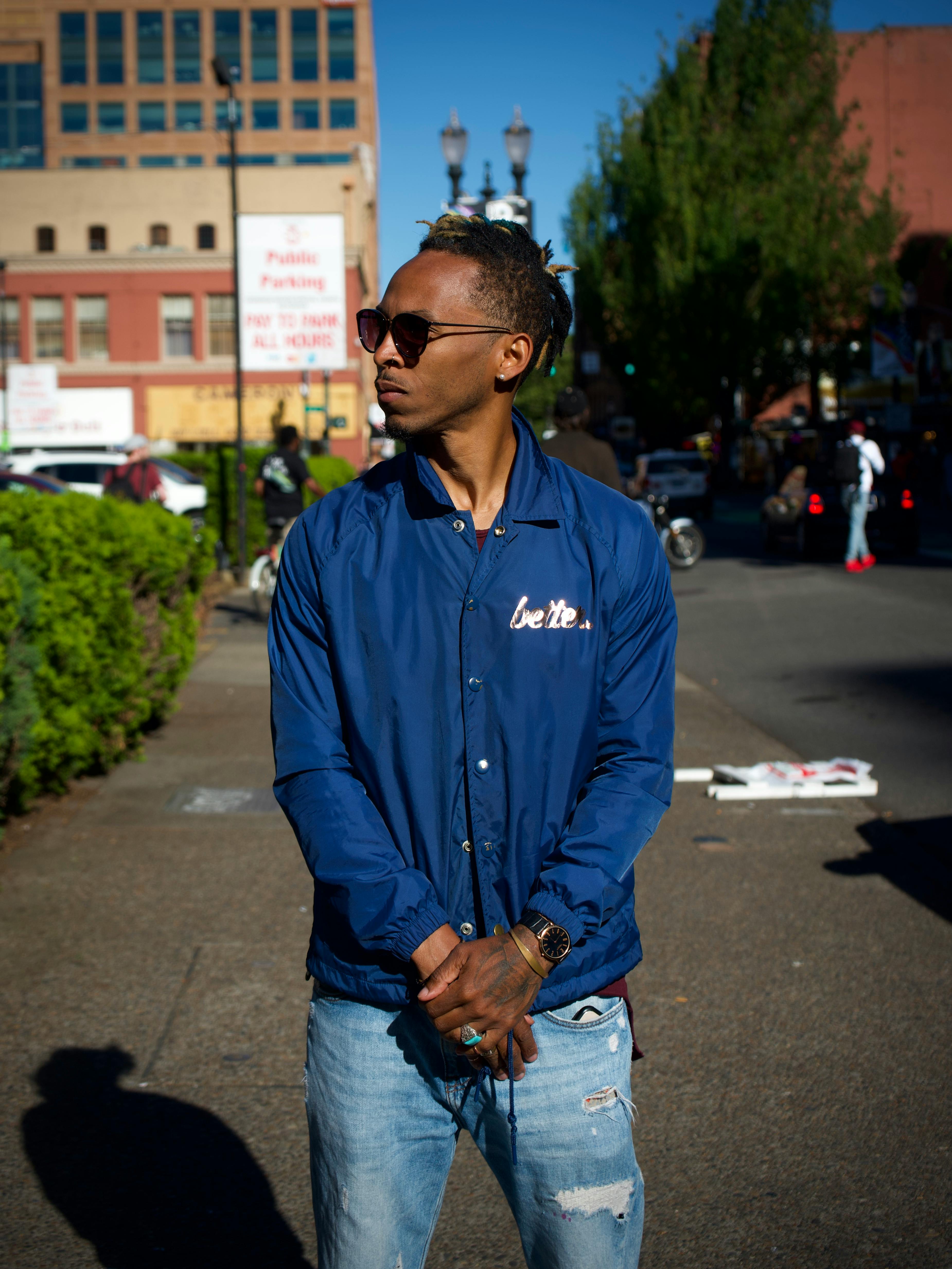 一位时尚的年轻人穿着蓝色夹克，戴着墨镜，站在充满活力的城市街头