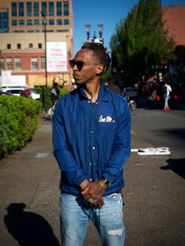 一位时尚的年轻人穿着蓝色夹克，戴着墨镜，站在充满活力的城市街头