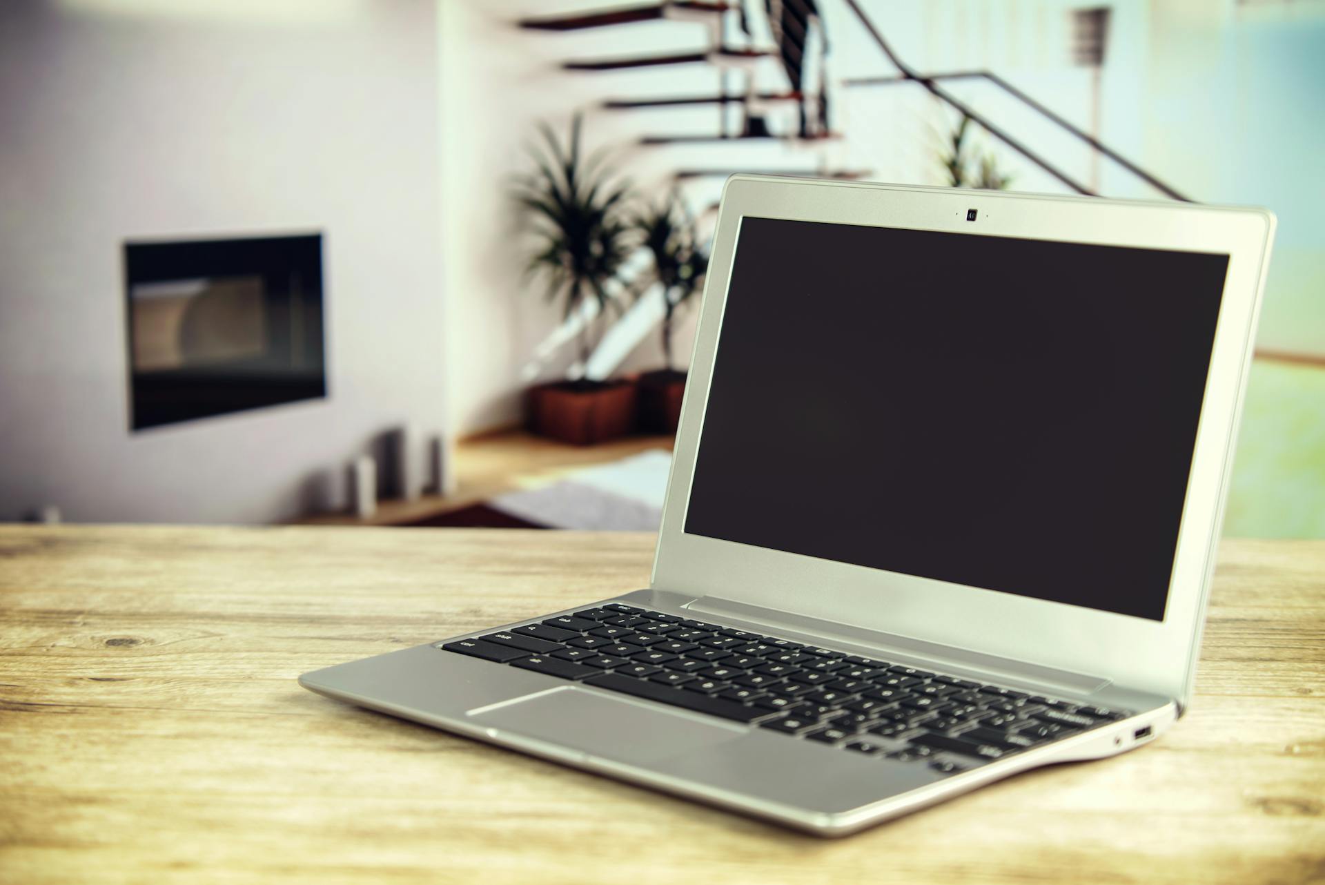 Sleek laptop on a wooden desk with blurred contemporary home interior in the background.