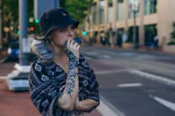 一名戴着黑色水桶帽的纹身女子若有所思地站在城市街道上，展现着都市时尚