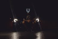 一张忧郁的照片中，一个戴着未来派面具的人在夜间被汽车前灯照亮