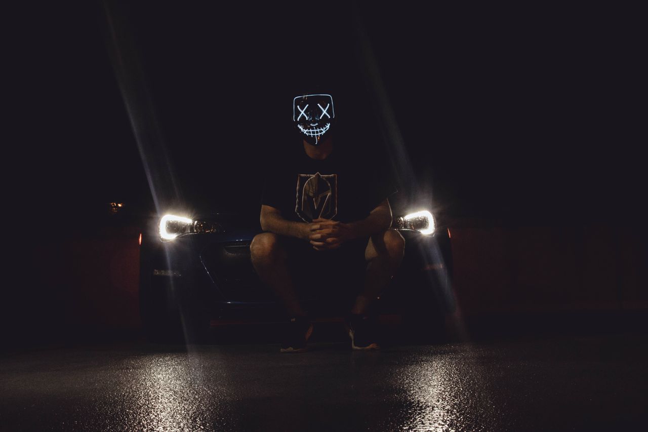 moody shot of a person in a futuristic mask illuminated by car headlig